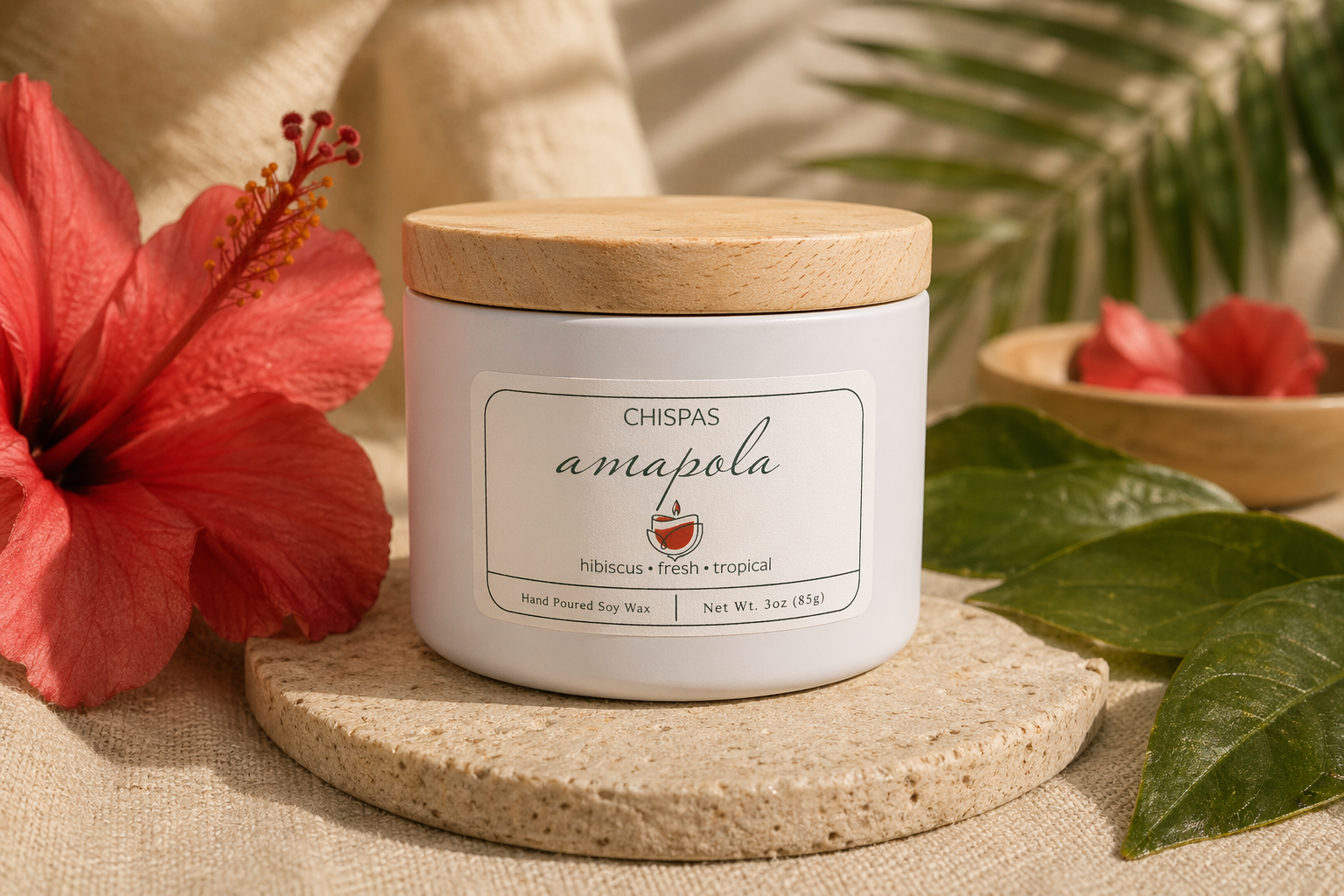 Amapola candle by Chispas with a wooden lid, styled with hibiscus flower and green leaves on a warm natural surface.