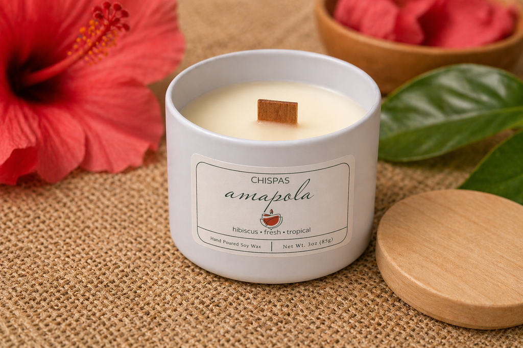 Amapola candle by Chispas with a wooden wick, styled with hibiscus flower and green leaves in a warm tropical setting.